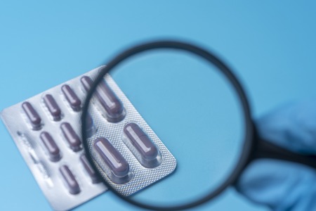 Hand holding magnifying magnifying glass over the bottle of pills on a blue background.の写真素材