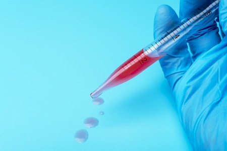 A gloved hand holding a laboratory pipette on a blue background.の写真素材