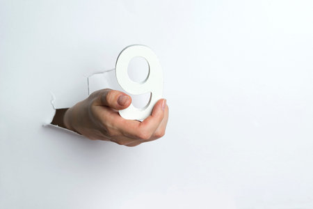 Female hand holds the number 9 on white background.