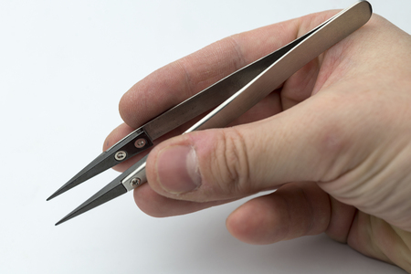 Hand holding tweezers on a white background.の写真素材