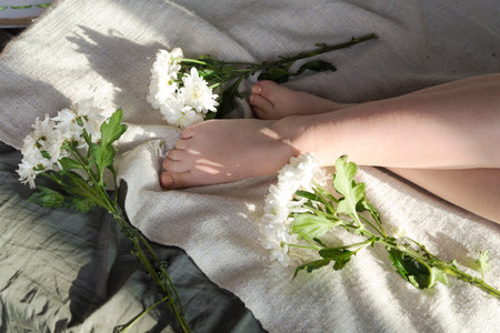Feet near the flowers on the bed.