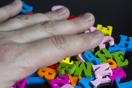A lot of colored letters on a black background with a hand.の写真素材