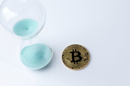 Gold bitcoin and hourglass on a white background.