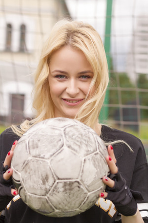 Beautiful blonde with a ball at the football goal. Football field at the gate close-up.の写真素材