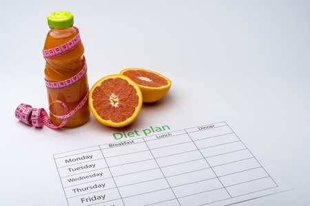 Diet plan and bottle of grapefruit juice with fresh grapefruit on white background. The concept of healthy eating.の写真素材