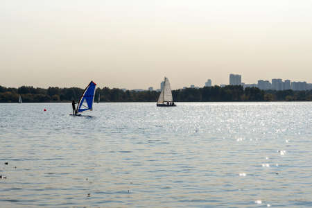 Windsurfer. Man is surfing on the background of skyscrapers. Man on a windsurf board. Windsurfing in the city. Water sports. Surfing with a sail.の写真素材