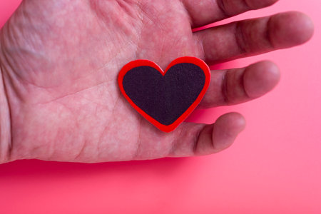 A man's hand holds a heart on an isolated pink background. Concept of Valentine's day and mother's day. The concept of love and loyalty.の写真素材