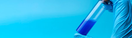 Close-up of glass tube with blue fluid in scientist hand during medical test. A gloved hand holds a flask of blue liquid.の写真素材