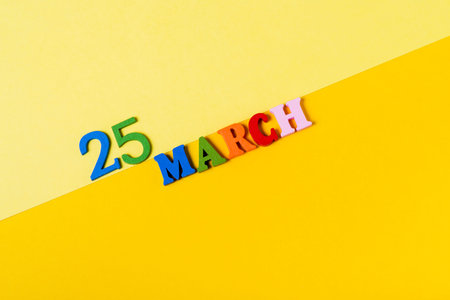 March 25, wooden letters on a yellow, paper background. The concept of the March 25 calendar.