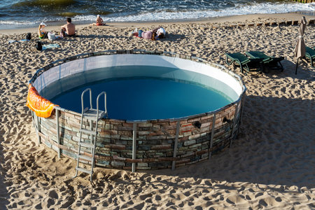 Round pool near the sea, on the beach for vacationers. The concept of recreation and entertainment.