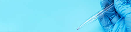 A gloved hand holding a laboratory pipette on a blue background. A place for text or design.の写真素材