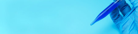 A gloved hand holds a lab pipette with blue liquid on a blue background. A place for text or design.の写真素材
