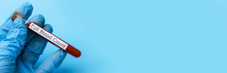 Hand Holding a Test for a Full blood Test in a test tube on a Blue Background. The concept of Medicine and Analysis. Copy spaceの写真素材