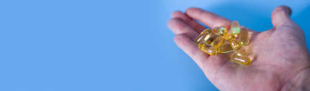 Hand holding omega-3 capsules on a blue background. Palm up, close-up. A high-resolution product. The concept of health. Copy Space.の写真素材