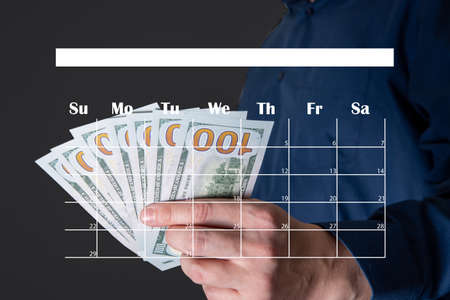 Money in the hands of a businessman and a calendar as an icon. Salary and bonus concept.の写真素材