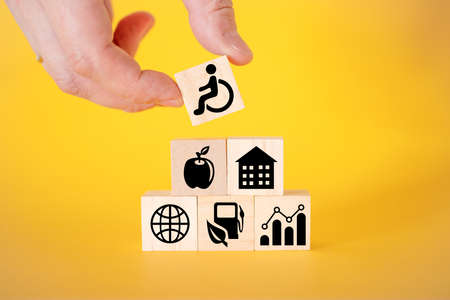 Icons for disabled people on wooden cubes, yellow background. The concept of assistance to the elderly and disabled.の写真素材