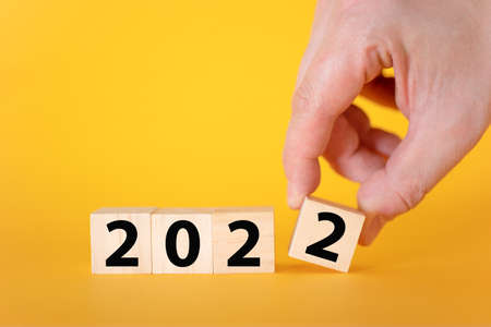 A hand holds a wooden cube blocks on a yellow background 2022. The concept of the New Year and holiday.の写真素材
