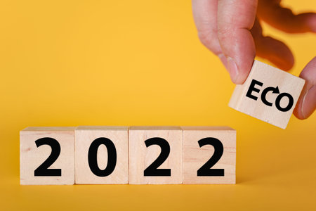 A hand holds wooden cubic blocks on a yellow background of 2022. The ecological year is 2022. The...