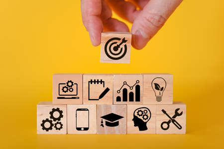 A business or economic growth concept with icons and goals on wooden cubes on a yellow background. Goals that are worth paying attention to.の写真素材