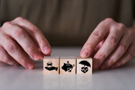 Close-up hand choose cube wooden toy blocks with insurance icon for safety family and health insurance. The concept of safe life.の写真素材