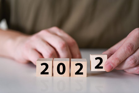 A businessman holds a wooden cubic block, for the year 2022. A new business year is changing and a...