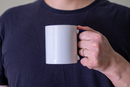Man holding a white cup of hot beverage outdoors. Man's hand holding a blank mug against black...