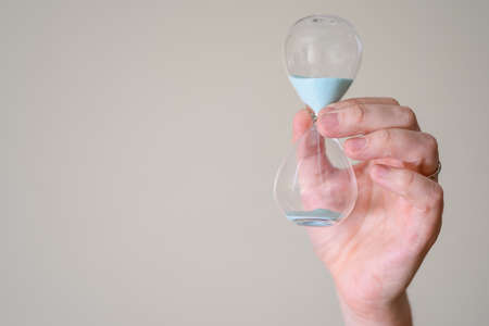 Hourglass in the hands of a man on a light background. The concept of time in your hands.の写真素材