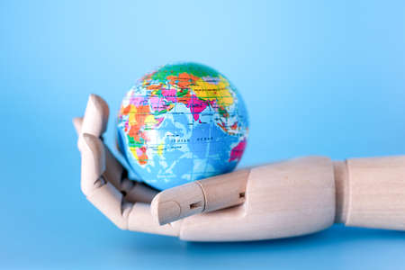 Close-up of a wooden hand holding a mini peace ball against a blue background. The concept of saving the Earth.の写真素材