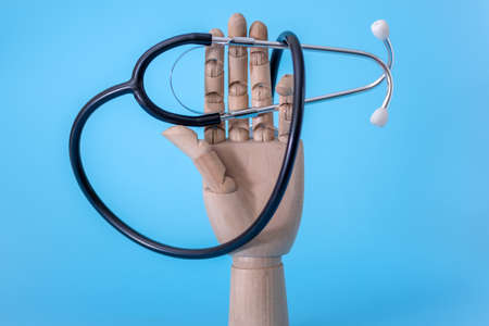 A wooden hand holds a stethoscope against a blue background. The concept of medicine and health care.の写真素材