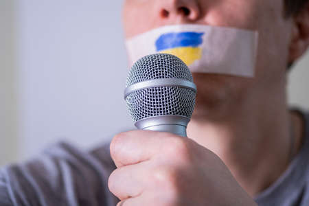 Caucasian man with duct tape on mouth. The flag of Ukraine on the tape. The concept of freedom of speech in world news.の写真素材