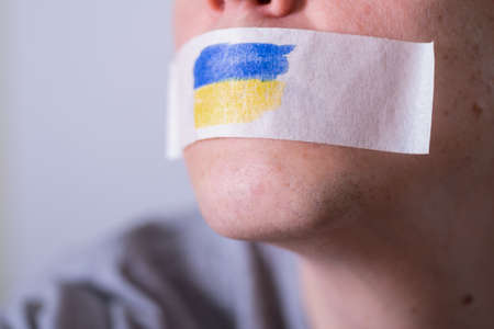 Caucasian man with duct tape on mouth. The flag of Ukraine on the tape. The concept of freedom of speech in world news.の写真素材