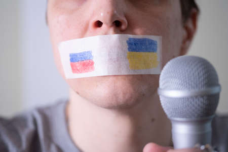 A duct-taped mouth with a flag of Russia and Ukraine trying to speak into a microphone. The concept of freedom of the press in Russia.の写真素材