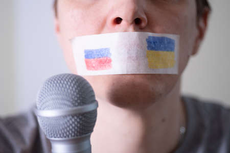 A duct-taped mouth with a flag of Russia and Ukraine trying to speak into a microphone. The concept of freedom of the press in Russia.の写真素材