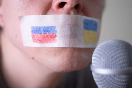 A duct-taped mouth with a flag of Russia and Ukraine trying to speak into a microphone. The concept of freedom of the press in Russia.の写真素材