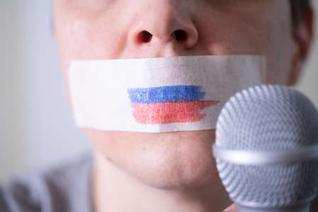 A duct-taped mouth with a Russian flag, trying to speak into a microphone. The concept of freedom of the press in Russia.の写真素材