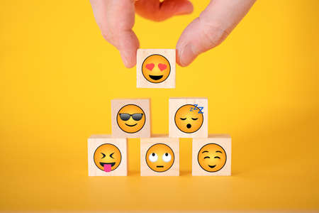 Close-up of a customer's hand selecting a smiley face with hearts instead of eyes on a wooden cube. World smiley day concept.の写真素材