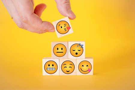 Close-up of a customer's hand selecting a smiley face with hearts instead of eyes on a wooden cube. World smiley day concept.の写真素材