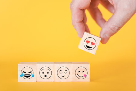 Close-up of a customer's hand selecting a smiley face with hearts instead of eyes on a wooden cube. World smiley day concept.の写真素材