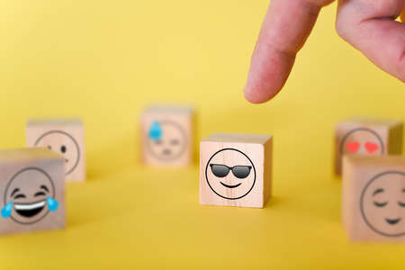 The finger points to a smiley emoji with glasses on a yellow background. The concept of the world day of emoticons.の写真素材