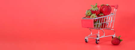 Small cart full of fresh ripe strawberries against a red background. Close-up, copyspace side view. Large healthy and tasty berry store conceptの写真素材