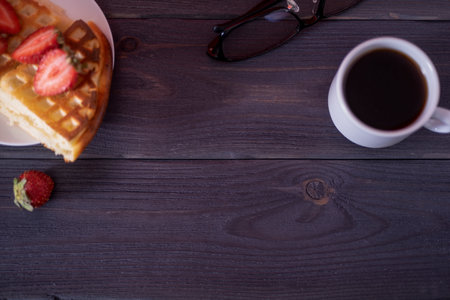 Belgian waffles with strawberries and coffee on a wooden, dark table. The concept of a delicious breakfast.の写真素材