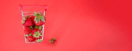 Small cart full of fresh ripe strawberries against a red background. Close-up, copyspace side view. Large healthy and tasty berry store conceptの写真素材