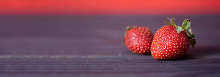 Two juicy strawberries lying on a wooden, dark background. High quality photo, healthy food concept.