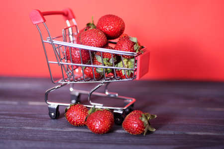Small cart full of fresh ripe strawberries against a red background. Close-up, copyspace side view. Large healthy and tasty berry store conceptの写真素材