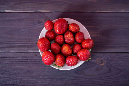 Fresh strawberries in a white plate on a dark wooden background. The concept of fresh and healthy food.の写真素材