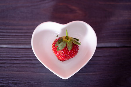 Strawberries in a heart-shaped plate on a wooden, dark background. The concept of delicious and healthy food.の写真素材