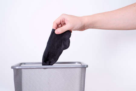 A man is throwing an old sock into a trash can with his hand against a white background. The concept of old clothes.の写真素材