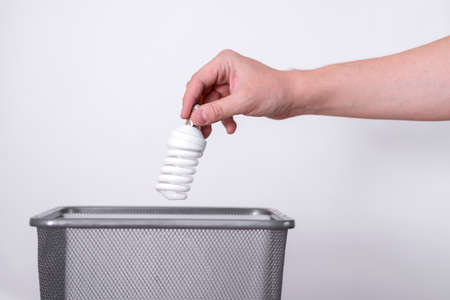 A hand throws a light bulb into a trash can against a gray background. The concept of eco-electricity.の写真素材