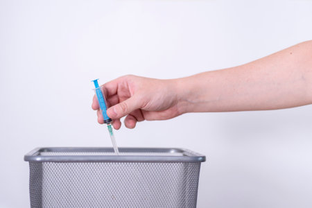 A hand tosses a used syringe in the trash on a gray background. The concept of medical waste disposal.の写真素材