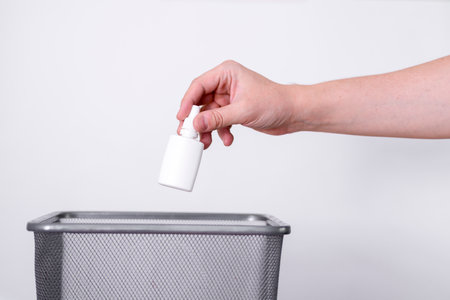 A hand throws a plastic tube into the trash against a gray background. A man's hand throws the tube away.の写真素材
